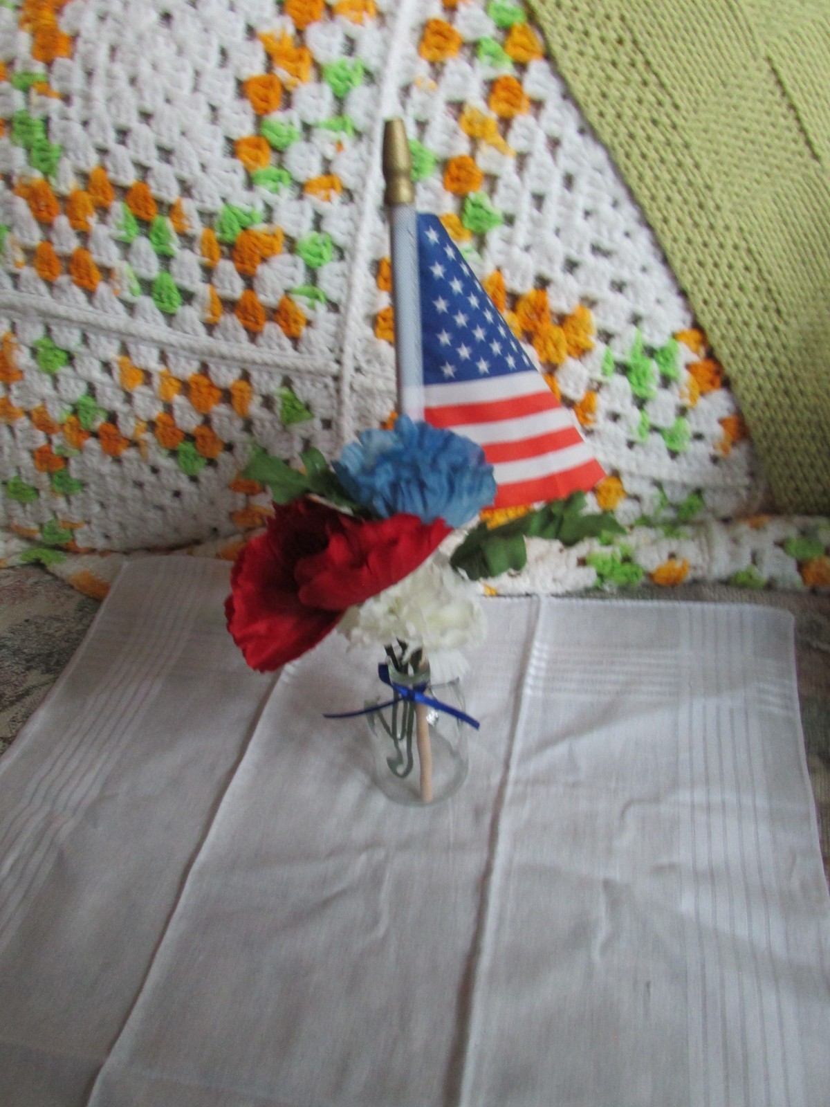 red, white, and blue fake flower bouquet, with small glass vase, and small flag