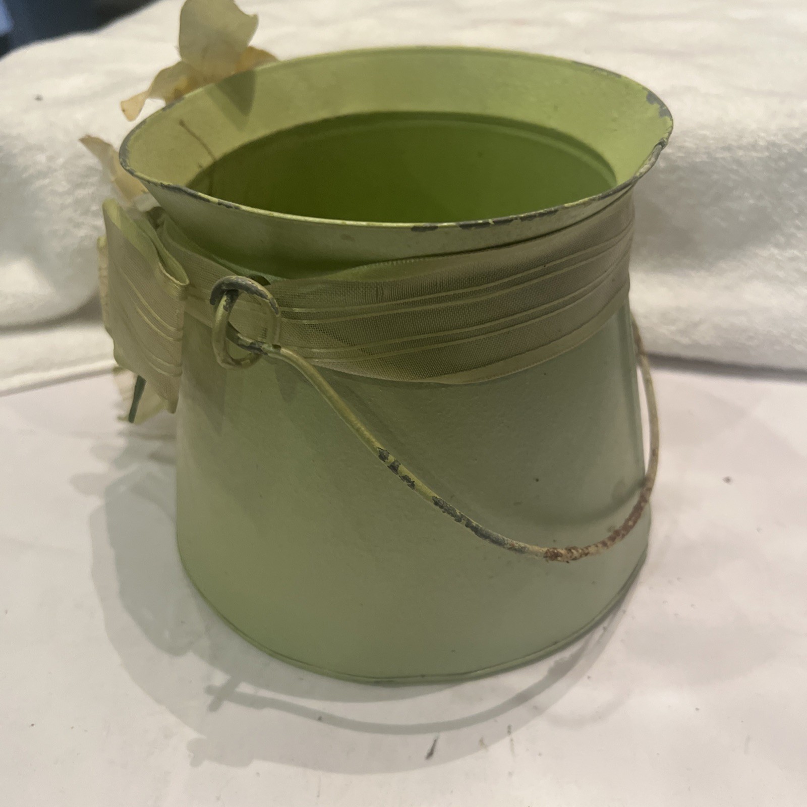 Green metal bucket decorated with a ribbon and artificial flowers