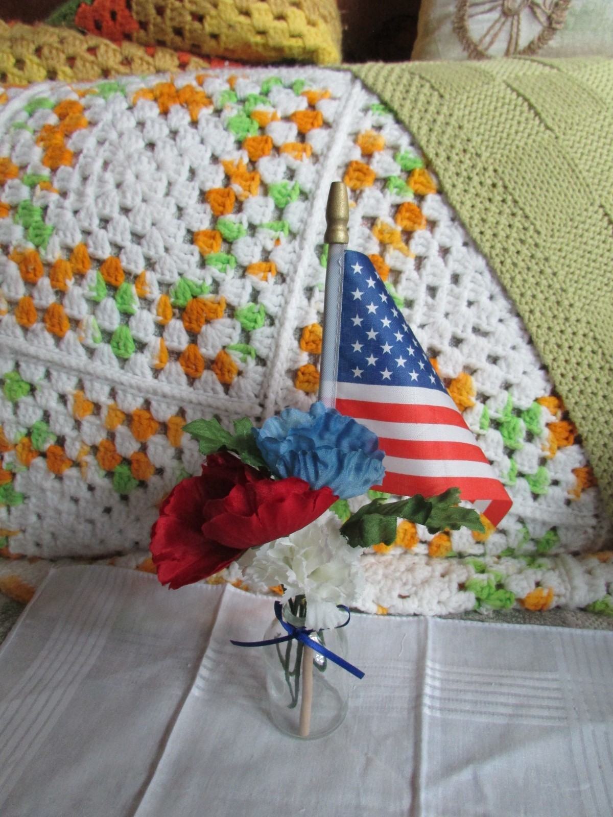 red, white, and blue fake flower bouquet, with small glass vase, and small flag