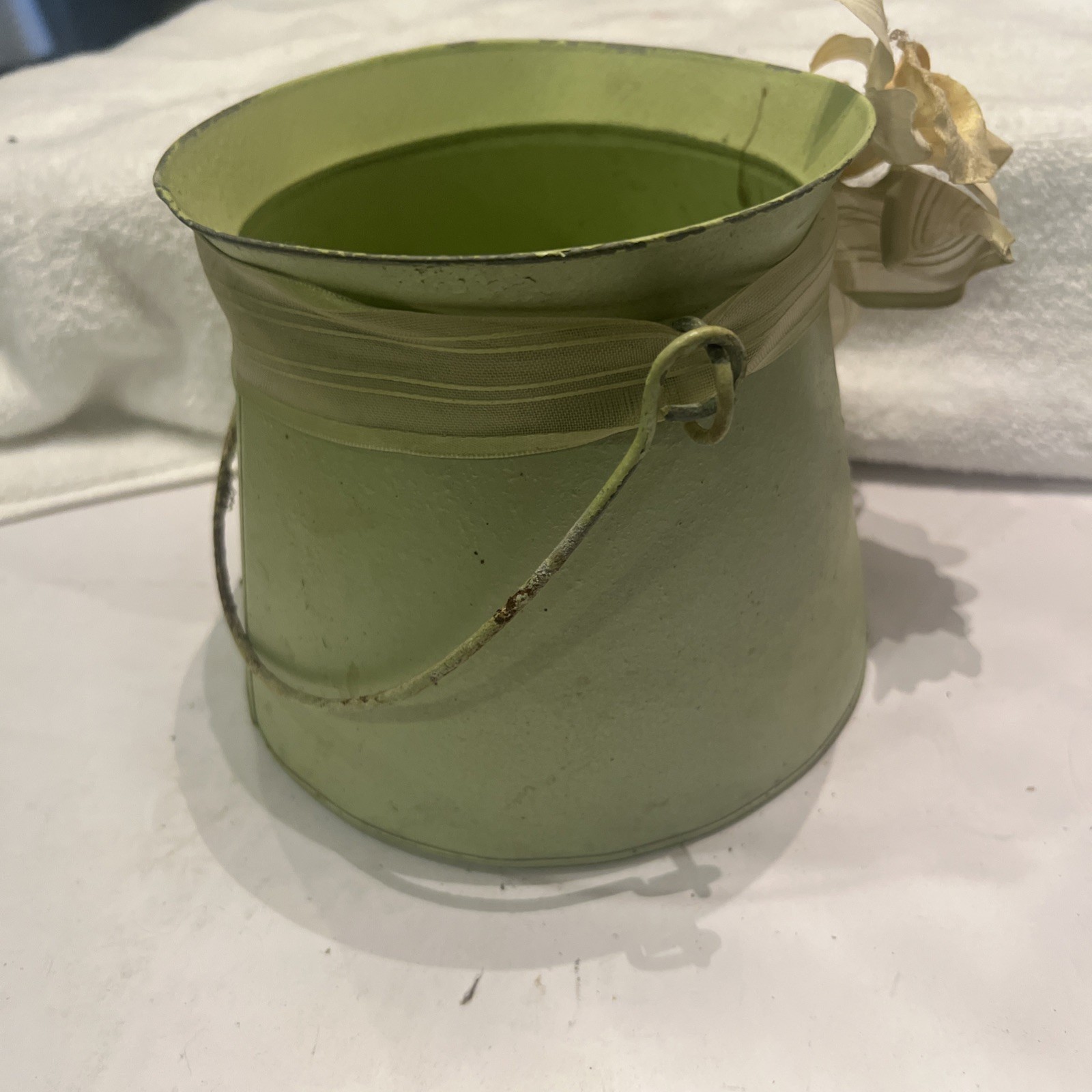 Green metal bucket decorated with a ribbon and artificial flowers