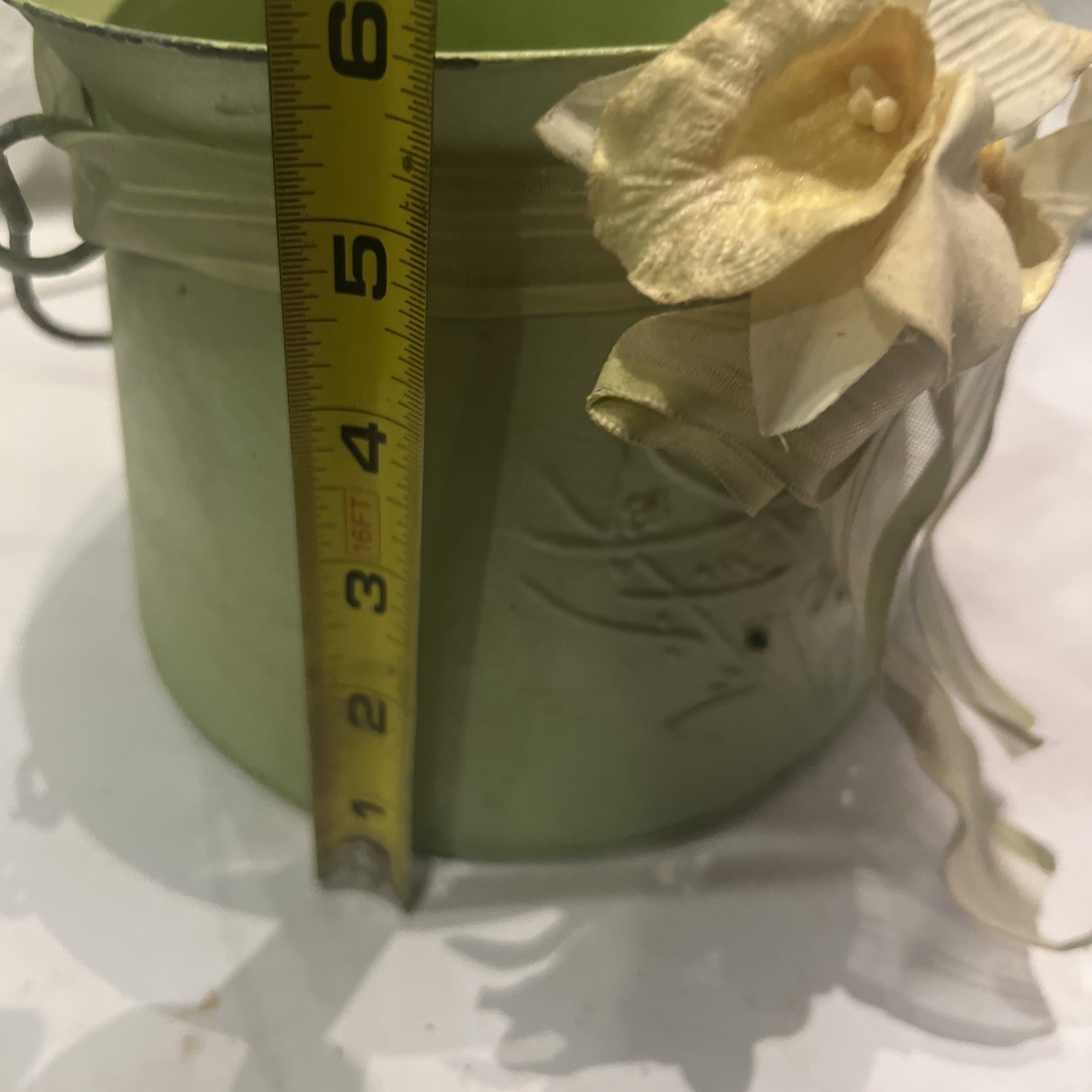 Green metal bucket decorated with a ribbon and artificial flowers