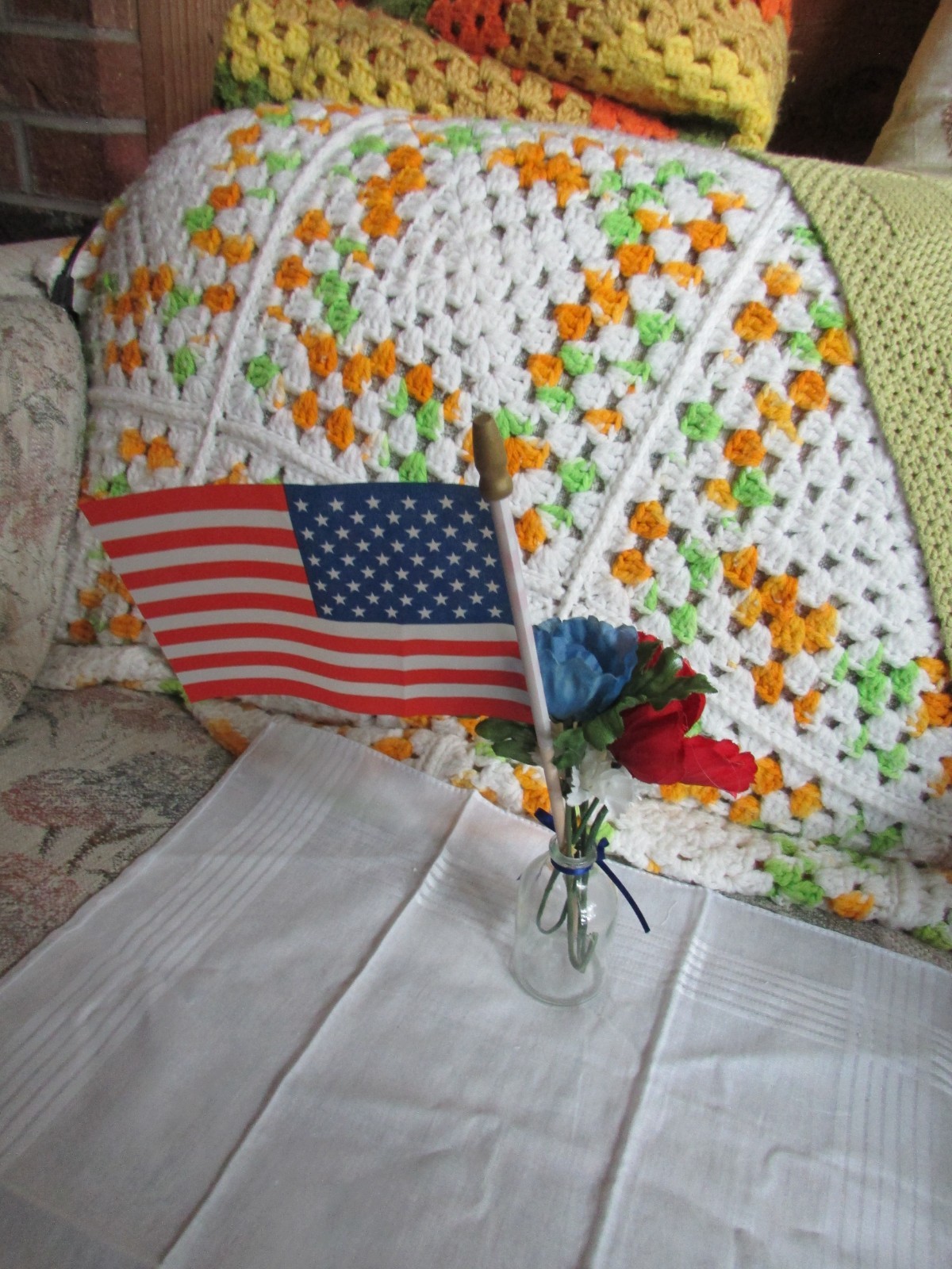red, white, and blue fake flower bouquet, with small glass vase, and small flag