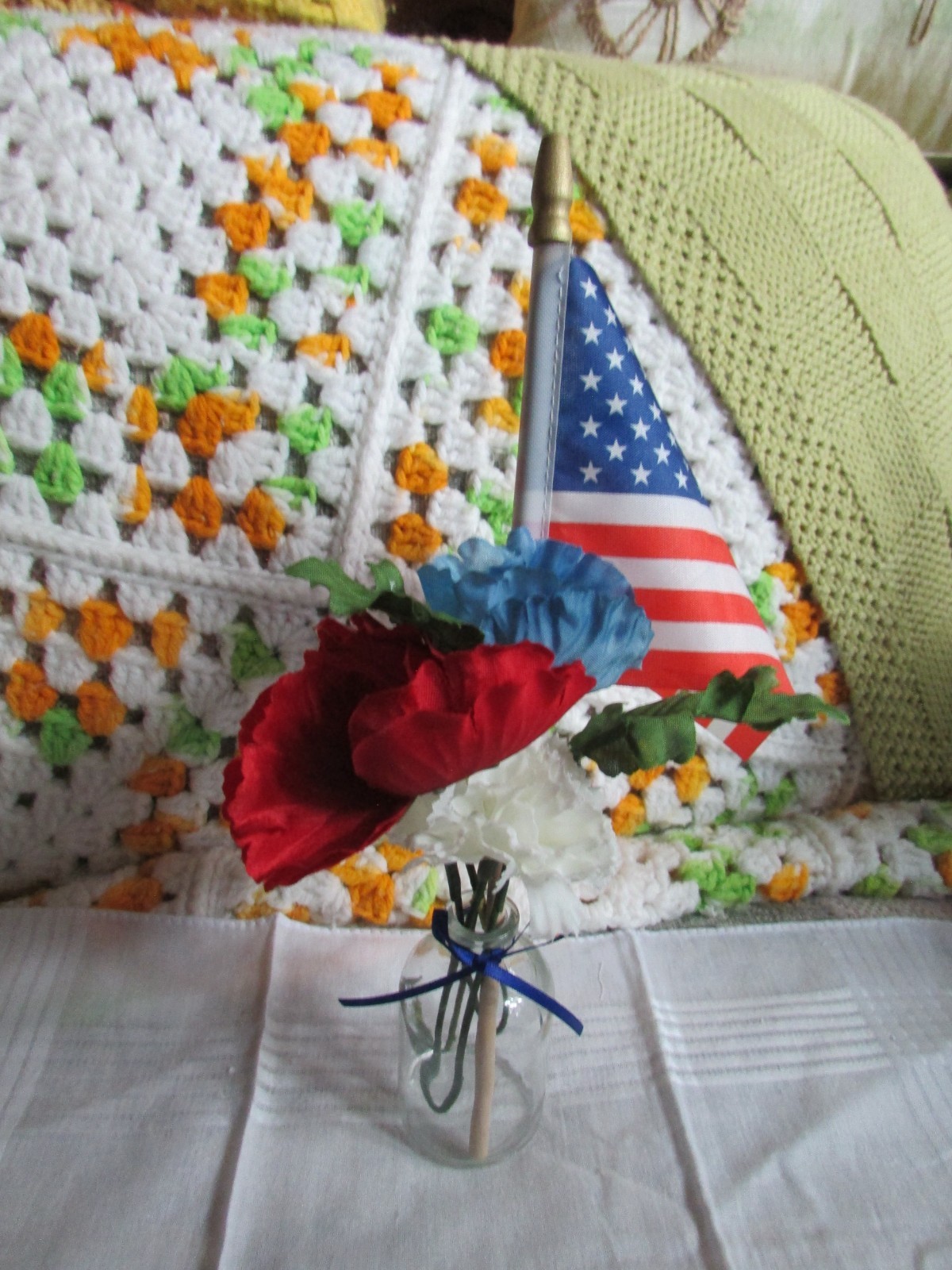 red, white, and blue fake flower bouquet, with small glass vase, and small flag