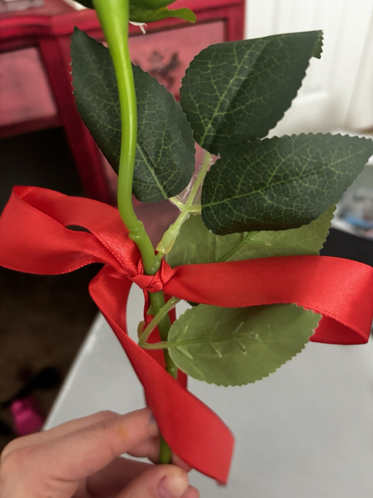 Faux White Rose With Green Stem And Leaves With Red Ribbon Tied Around Stem