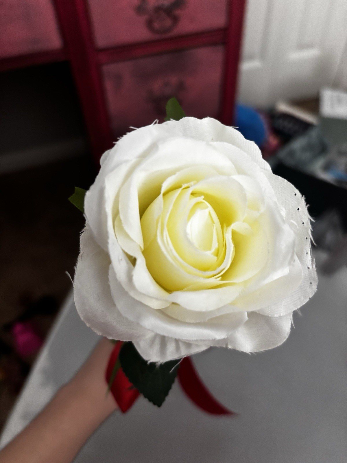 Faux White Rose With Green Stem And Leaves With Red Ribbon Tied Around Stem