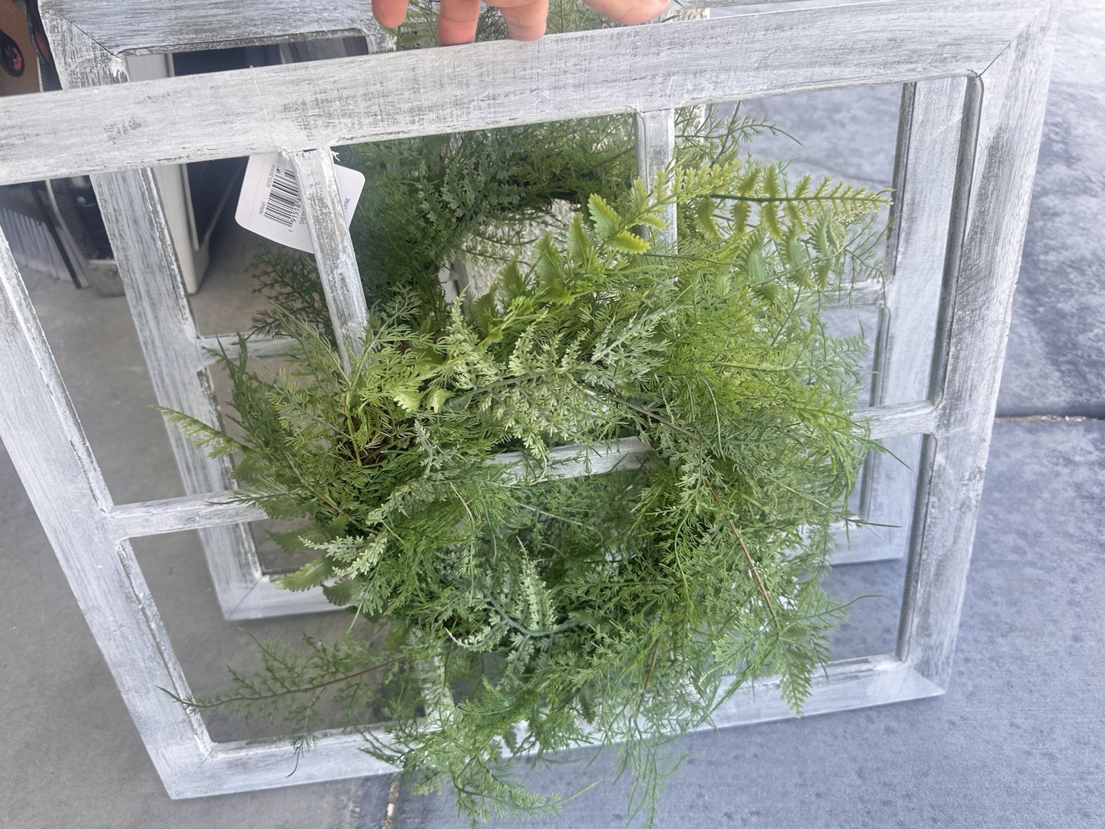 decor item features a faux asparagus fern wreath hung on a distressed,