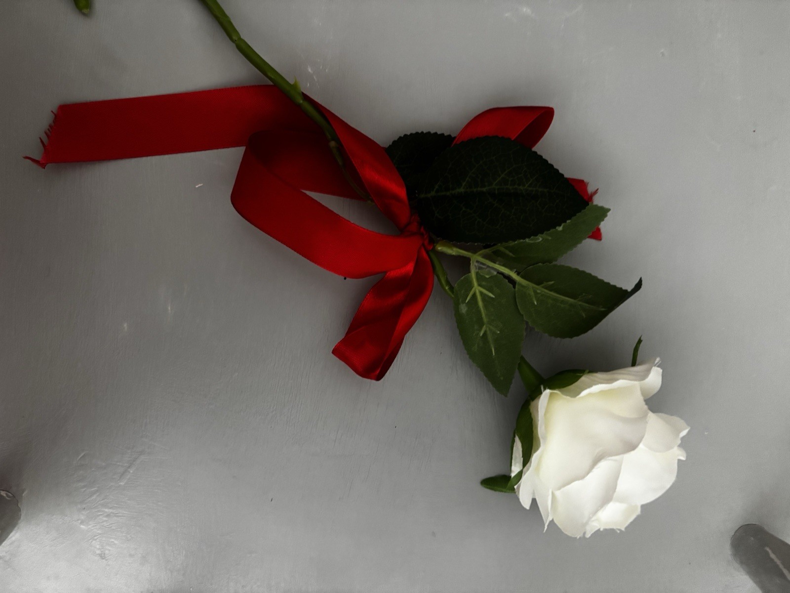 Faux White Rose With Green Stem And Leaves With Red Ribbon Tied Around Stem