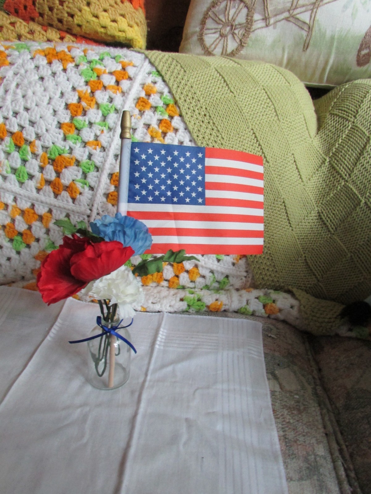 red, white, and blue fake flower bouquet, with small glass vase, and small flag