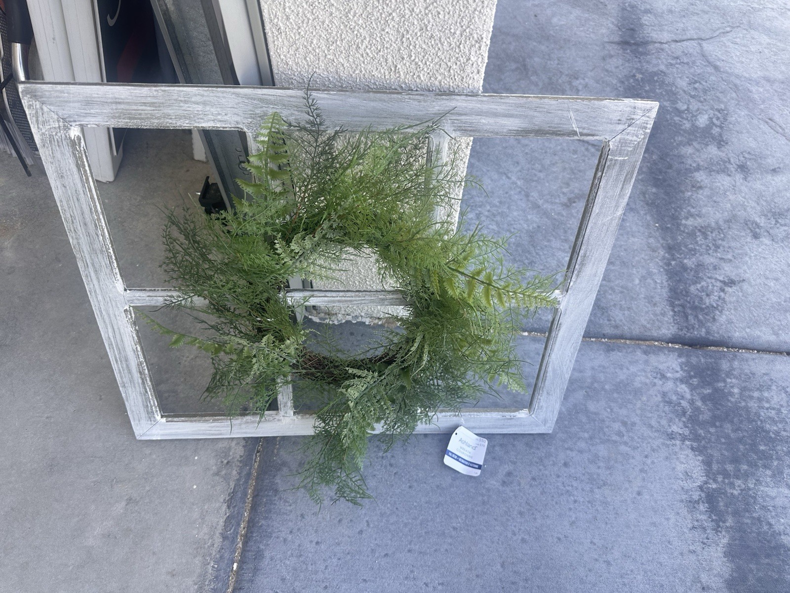 decor item features a faux asparagus fern wreath hung on a distressed,