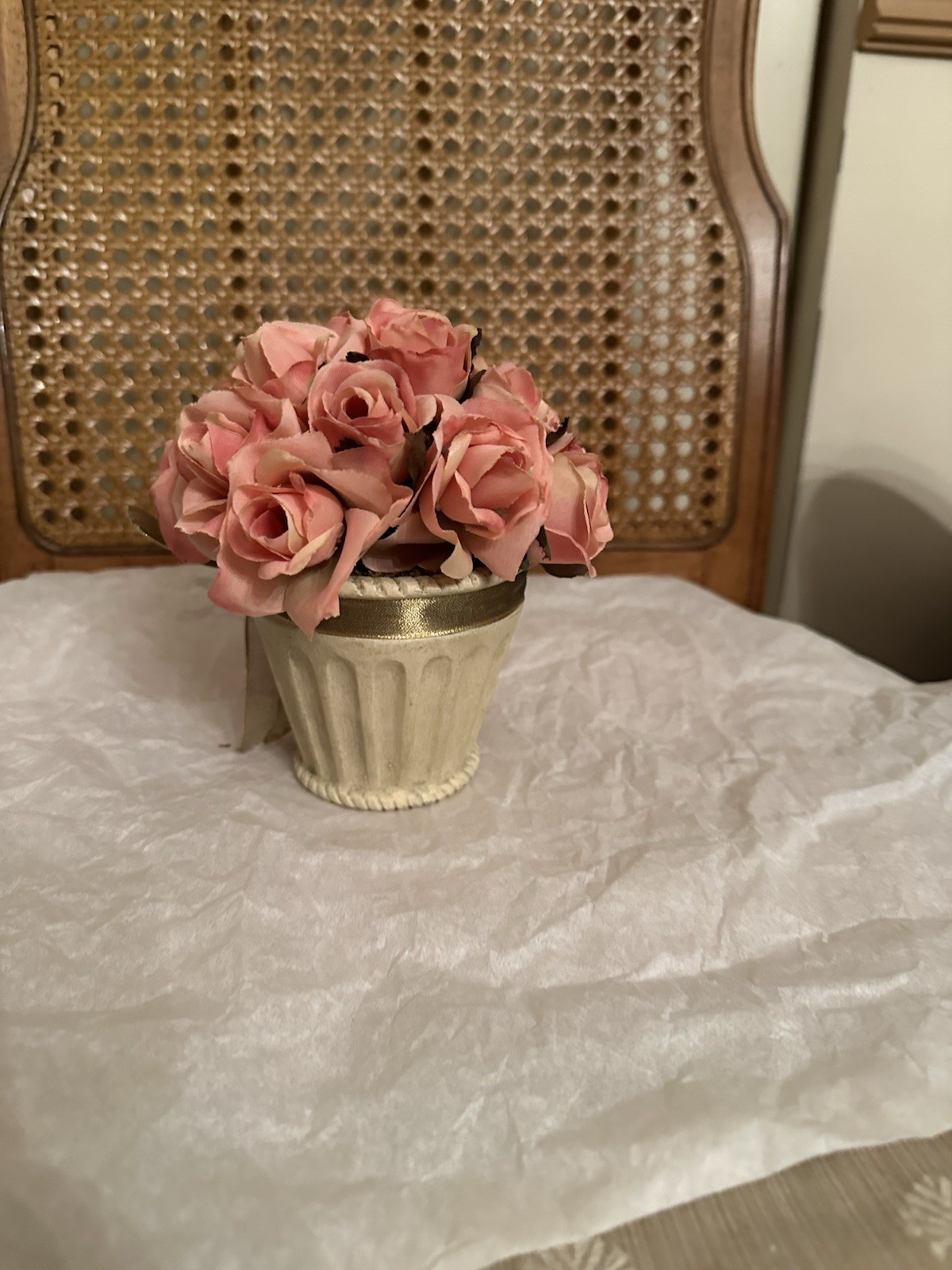 Artificial pink roses in a fluted cream vase with gold ribbon.