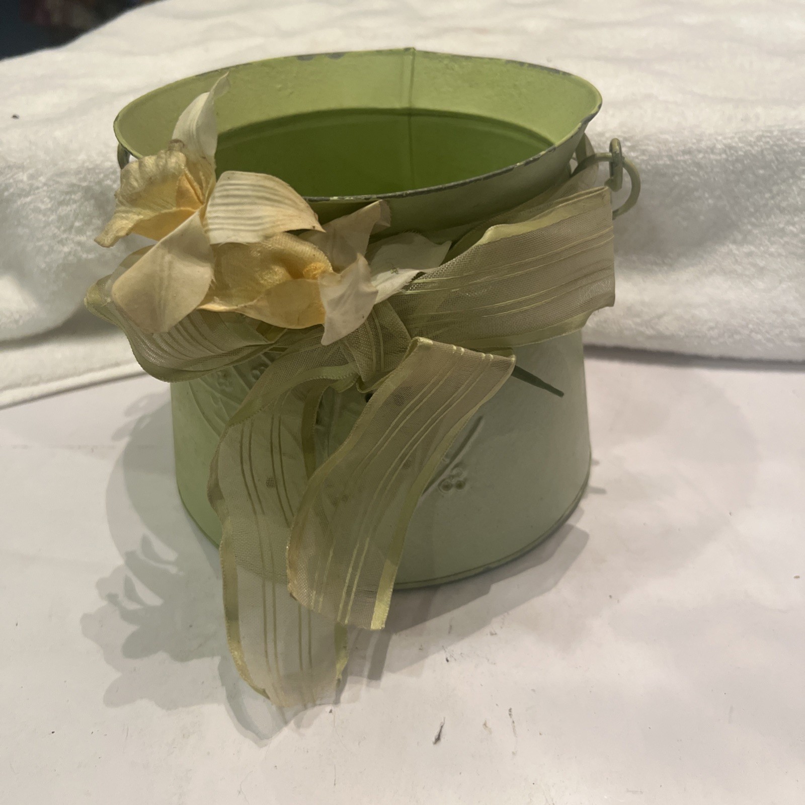 Green metal bucket decorated with a ribbon and artificial flowers