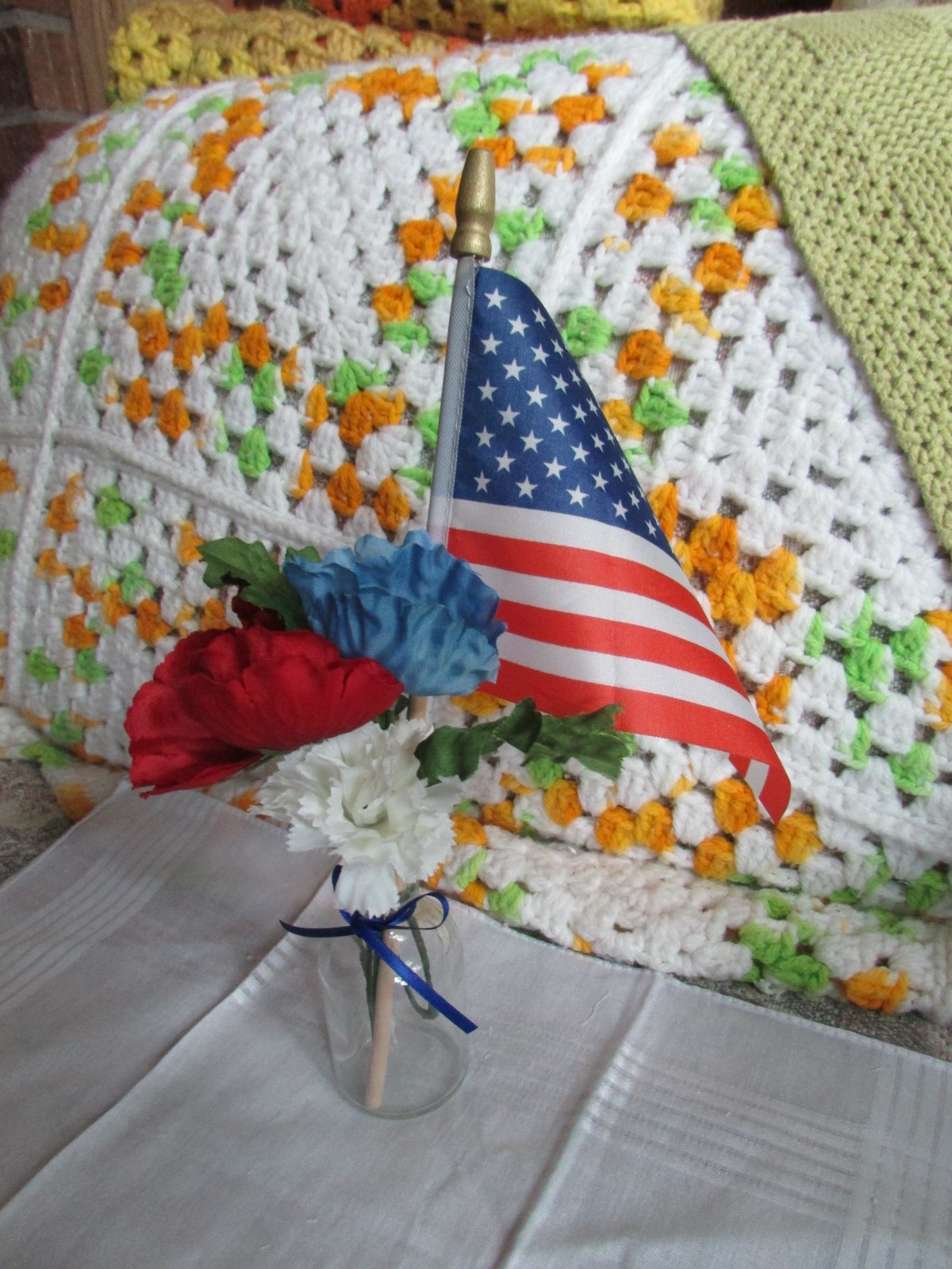 red, white, and blue fake flower bouquet, with small glass vase, and small flag